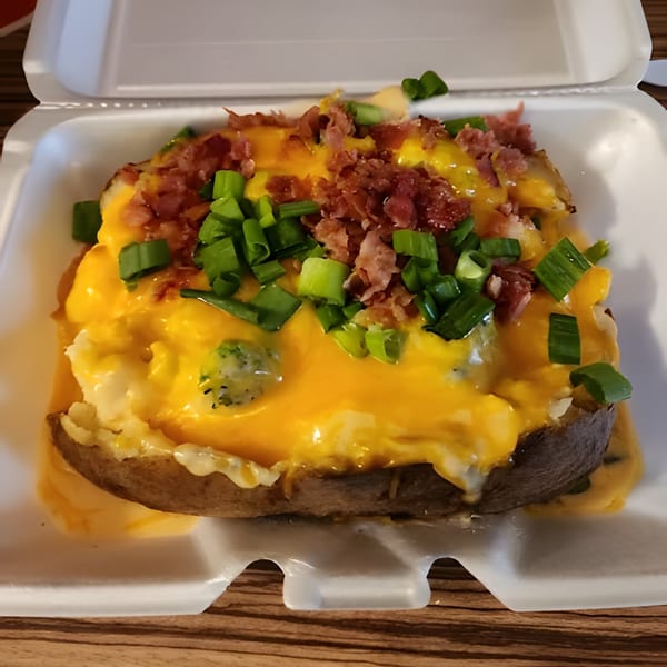 A loaded baked potato from The Spud Spot, topped with melted cheese, bacon bits, and green onions.