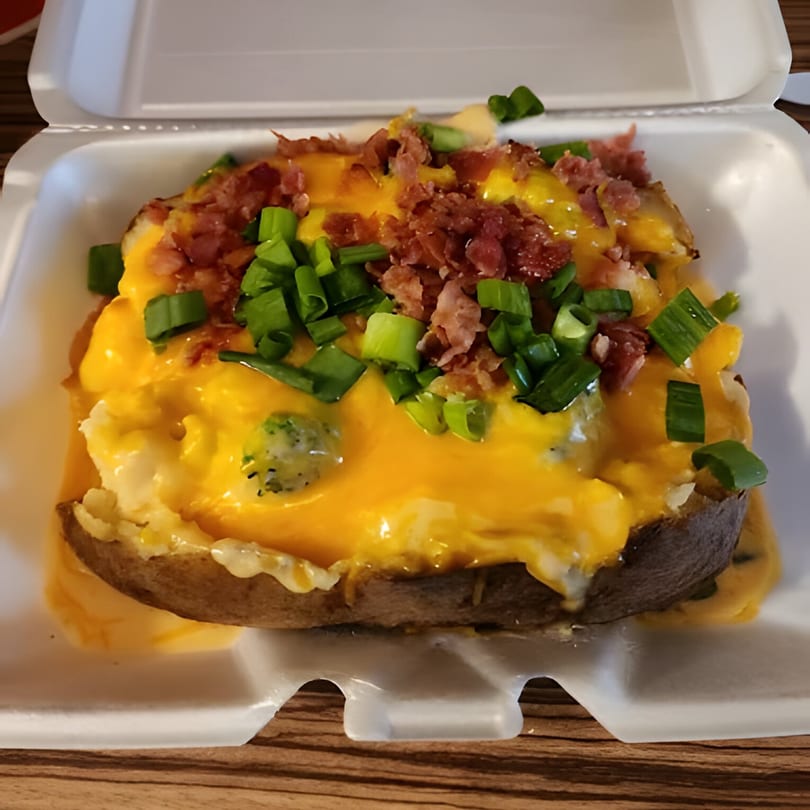 A loaded baked potato from The Spud Spot, topped with melted cheese, bacon bits, and green onions.