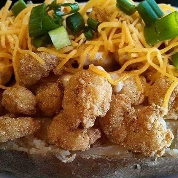 Baked potato topped with fried shrimp, shredded cheese, and chopped green onions.