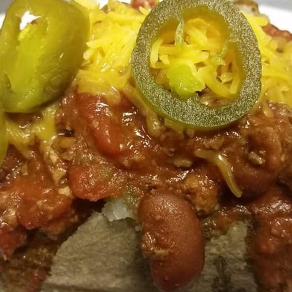 Close-up of a loaded baked potato with chili, shredded cheese, and sliced jalapeños.