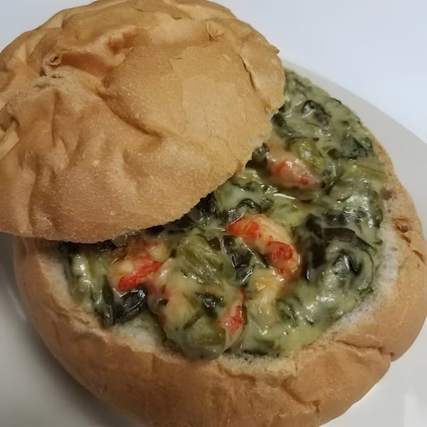 A bread bowl filled with creamy green spinach and shrimp, with a bread lid resting on top.